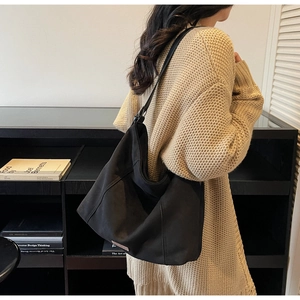 Detail of a large black suede tote bag with a slouchy hobo design worn on a shoulder