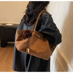 Close-up of brown suede tote bag with decorative dark fur pom-pom and wooden beads