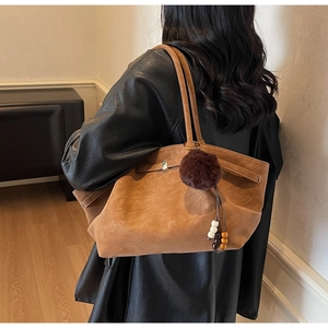 Close-up of brown suede tote bag with plush pompom and bead charm detail on model