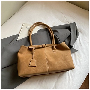 Detailed view of a brown suede tote bag with decorative buckles in a home office setting