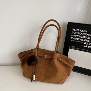 Detail view of brown faux suede tote bag with decorative fur pompom and beaded charm