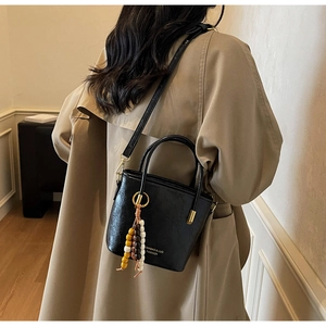 Dettaglio di borsa a secchiello in pelle PU nera con texture vintage e nappa in legno