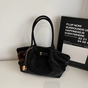 Close-up of black suede tote bag with brown pompom and wooden bead tassel detail