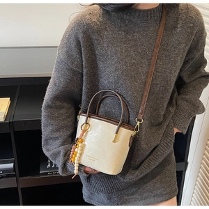 Dettaglio della borsa a secchiello beige retrò con manico marrone e nappa decorativa