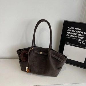 Detail of dark brown faux suede tote bag featuring a plush pom-pom and beaded tassel