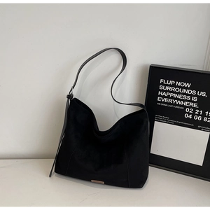 Detail view of the black suede hobo bag featuring a small brown leather logo and adjustable strap