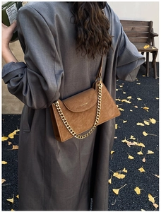 Detail of a brown matte leather crossbody bag featuring a gold chain and autumn street style