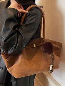Brown suede tote bag with plush charm and wooden beads worn by a model in a leather jacket