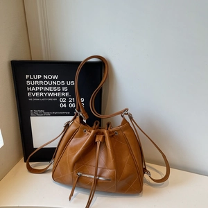 Detail of caramel quilted bucket bag showing decorative zipper and drawstring closure