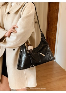 Détail du sac hobo minimaliste en cuir verni noir avec pompon en peluche et texture rétro