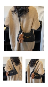 Close-up of black retro underarm bag with gold metal trim and brown plush bear charm