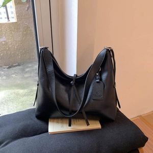 Gros plan d'un sac cabas en cuir noir avec étiquette logo sur un coussin et un livre