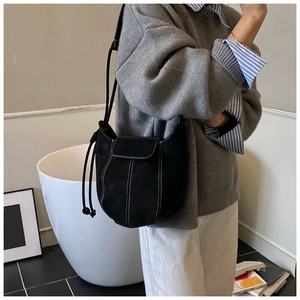 Detail of black matte suede bucket bag featuring contrast white stitching and drawstring