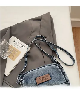 Détail d'un sac bandoulière en jean avec écusson logo en cuir marron et sangle souple