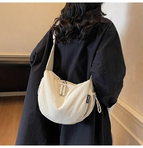 Dettaglio della borsa a mezzaluna beige con trama a pieghe e tracolla larga regolabile