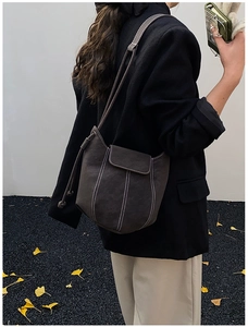 Close-up of brown suede bucket bag featuring white contrast stitching and drawstring detail