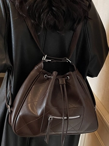 Deep brown quilted leather backpack tote with drawstring closure on model in black jacket