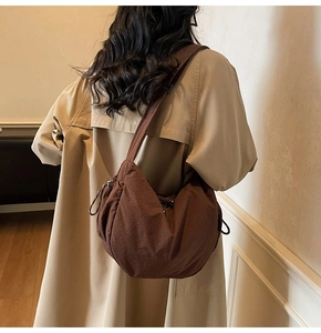 Dettaglio della trama del sacchetto a mezzaluna in nylon marrone scuro plissettato sulla spalla