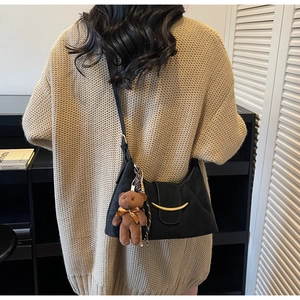 Detail of black suede shoulder bag with gold crescent buckle and plush bear charm