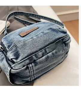 Détail du sac bandoulière en jean bleu avec délavage vintage et écusson logo en cuir brun