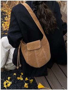 Close-up of brown suede bucket bag featuring contrast white stitching and drawstring detail