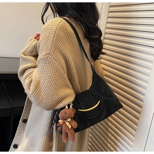 Detail of black leather underarm bag with gold crescent moon buckle and bear charm