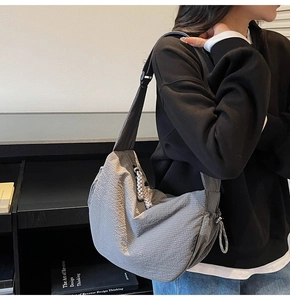 Dettaglio della borsa a mezzaluna grigia con tirante intrecciato e tracolla regolabile