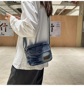Gros plan du sac bandoulière en denim délavé rétro avec bouton métal et logo en cuir