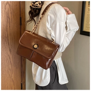 Detail of a brown patent leather crossbody bag with gold chain strap and rotary lock