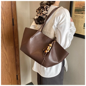 Detail view of large dark brown oil-wax leather tote bag with stylish wooden bead pendant