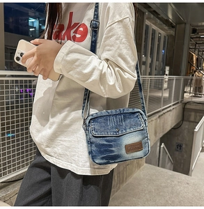 Détail d'un sac bandoulière en denim délavé vintage avec logo en cuir marron et rabat chic