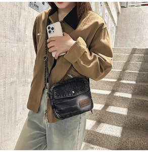 Détail d'un sac bandoulière en denim noir délavé avec un écusson en cuir marron à l'avant