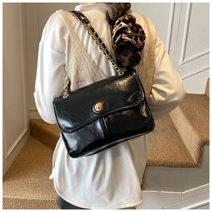 Detail of elegant black glossy crossbody bag featuring amber gold buckle and chain strap