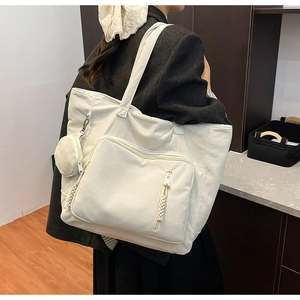 Dettaglio della borsa tote in velluto a coste bianco crema con tasca frontale e ciondolo