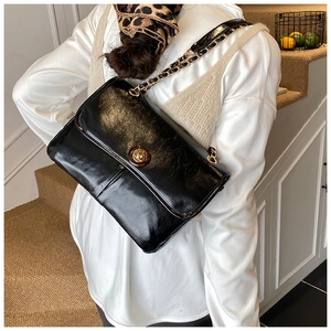 Close-up of elegant black glossy leather bag with gold chain strap on a model