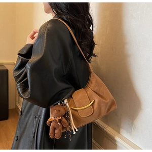 Detail of a brown half-moon hobo bag with a gold crescent buckle and plush bear charm