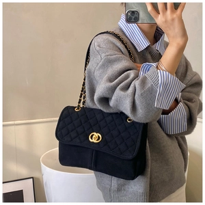 Détail du sac matelassé noir avec chaîne dorée et boucle sur un pull-over gris