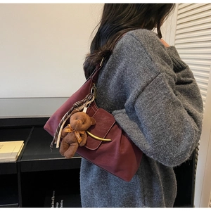 Detail view of burgundy pleated underarm bag with golden crescent buckle and cute bear charm
