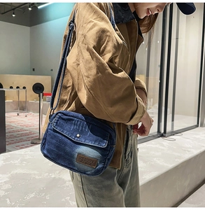 Détail du sac bandoulière en denim bleu avec étiquette en cuir brun et sangle réglable