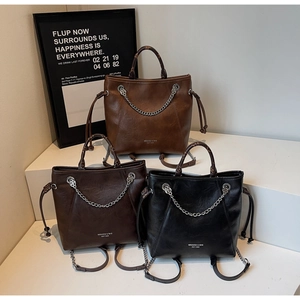 Tre eleganti borse tote con catene in marrone, caffè e nero su un supporto bianco