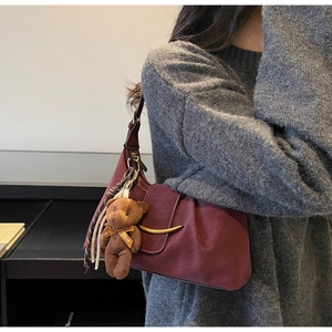 Detail of dark red pleated underarm bag with gold horn buckle and teddy bear charm on model