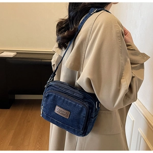 Vue détaillée du sac bandoulière en jean bleu foncé avec fermetures et écusson logo