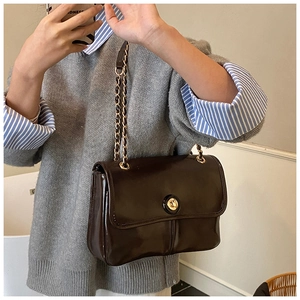Detail of dark chocolate glossy leather bag with gold circular clasp and chain strap