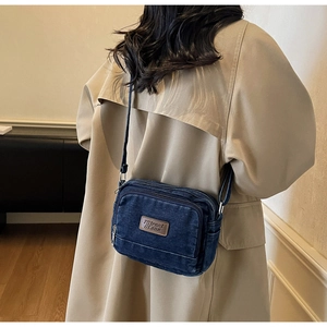 Vue détaillée d'un sac bandoulière en denim bleu foncé avec compartiments zippés et étiquette
