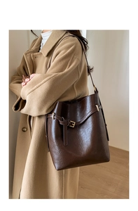 Détail du sac seau en cuir marron foncé avec boucles dorées sur un manteau camel