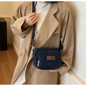 Détail du sac bandoulière en denim bleu avec plusieurs poches zippées et sangle réglable