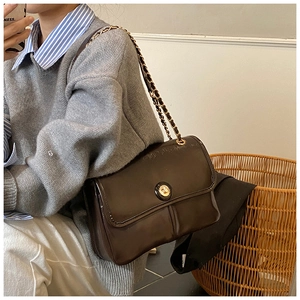 Detail of a dark brown glossy leather crossbody bag with golden chain and round clasp buckle