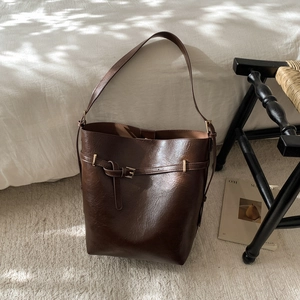 Détail d'un sac seau marron foncé en cuir synthétique brillant avec une boucle dorée