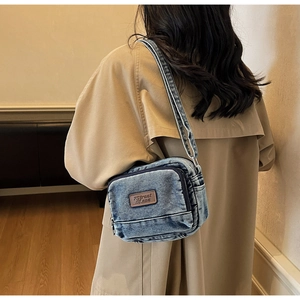Vue détaillée du sac bandoulière en denim bleu délavé avec étiquette en cuir et bandoulière
