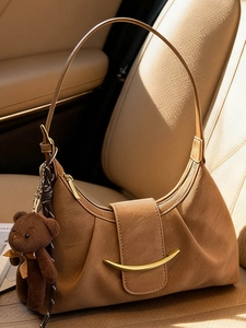 Brown hobo underarm bag with gold metal buckle and cute bear charm on a car seat